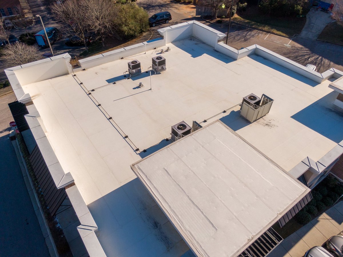 Drone aerial view of commercial and industrial buildings with white TPO flat roofing systems, rooftop HVAC units, and detailed architectural layouts under bright daylight