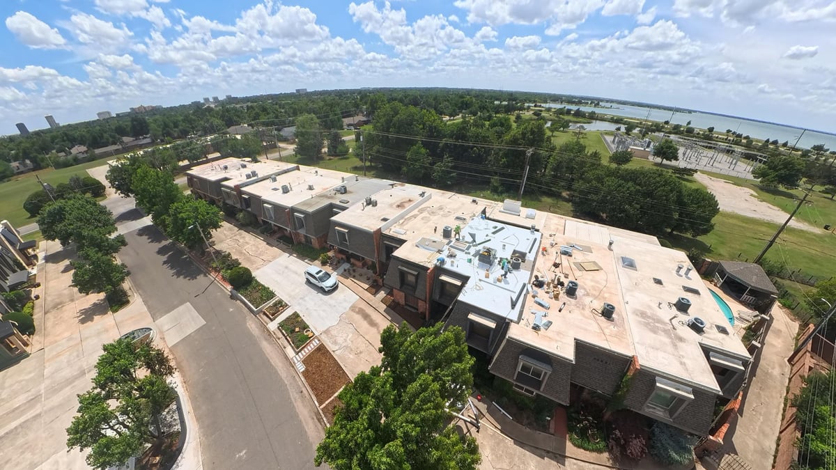 Aerial view of modern residential development under construction with multiple buildings, surrounding green landscape, and waterway visible in distance