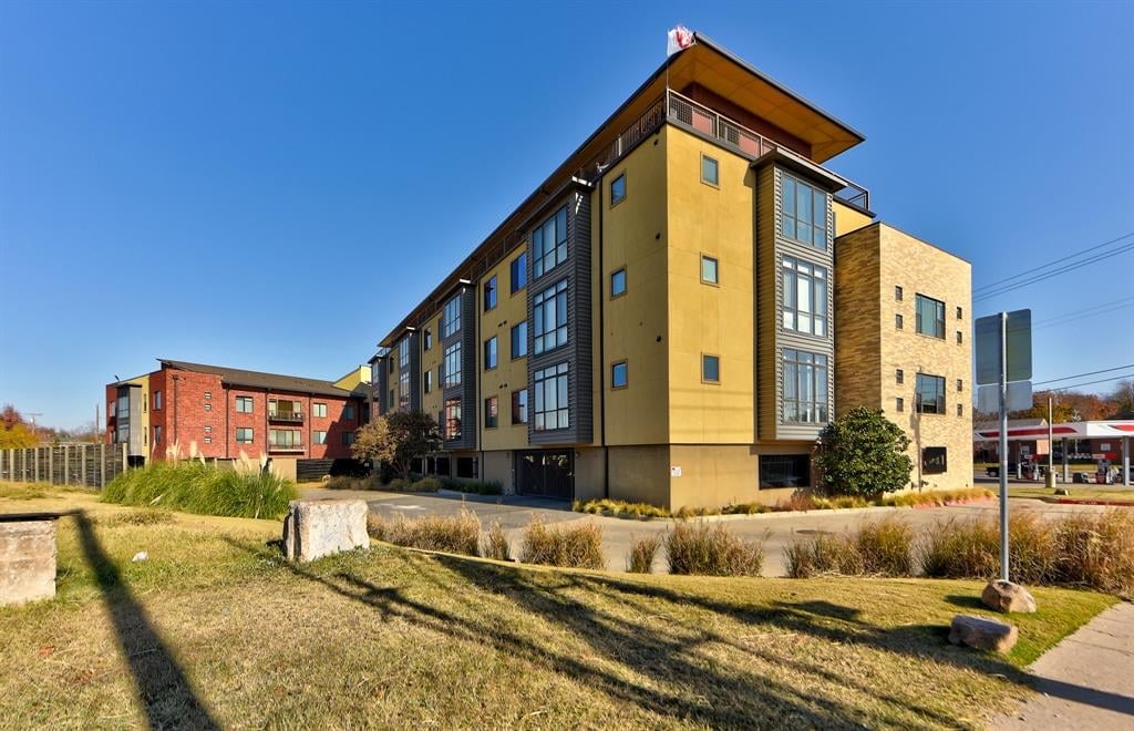 Modern multi-story residential building with yellow and blue facade on a sunny day with clear blue sky and landscaped grounds