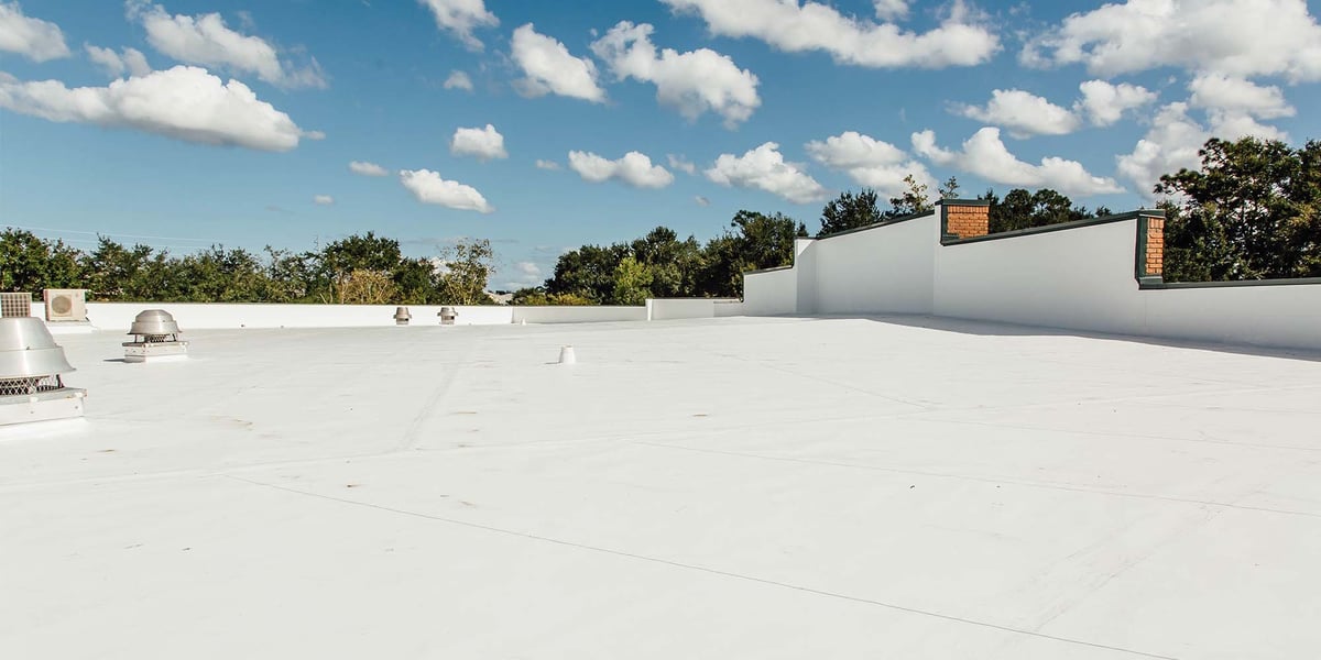 Flat white commercial rooftop with HVAC units under blue sky with white clouds and surrounding trees