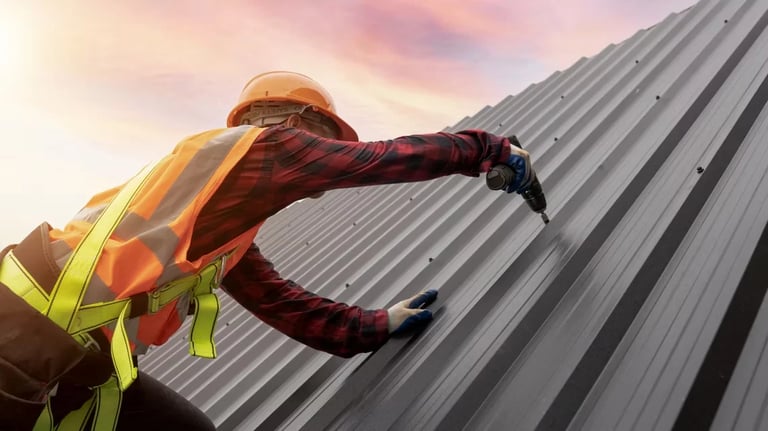 Construction worker in safety gear working on metal roof panels against sunset sky